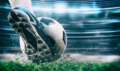 Football scene at night match with close up of a soccer shoe hitting the ball with power