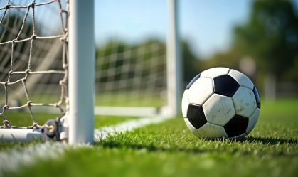 Soccer ball lies near soccer goal on grassy field. Daytime shot. Sport recreation concept. Photo captures active lifestyle. Great for sports websites and blogs.