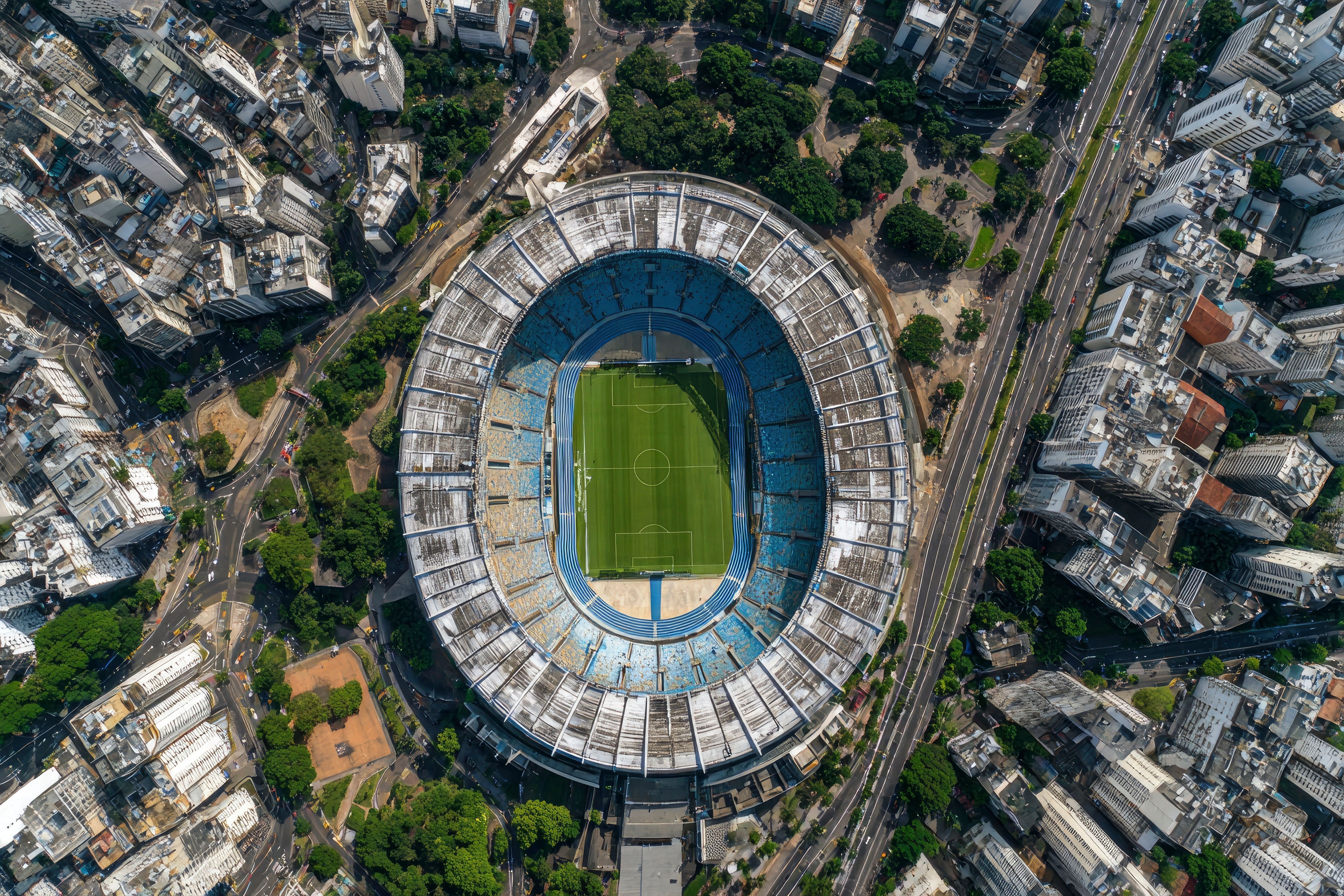 Aerial view of a stadium in a cityscape featuring green field blue seating and surrounding buildings