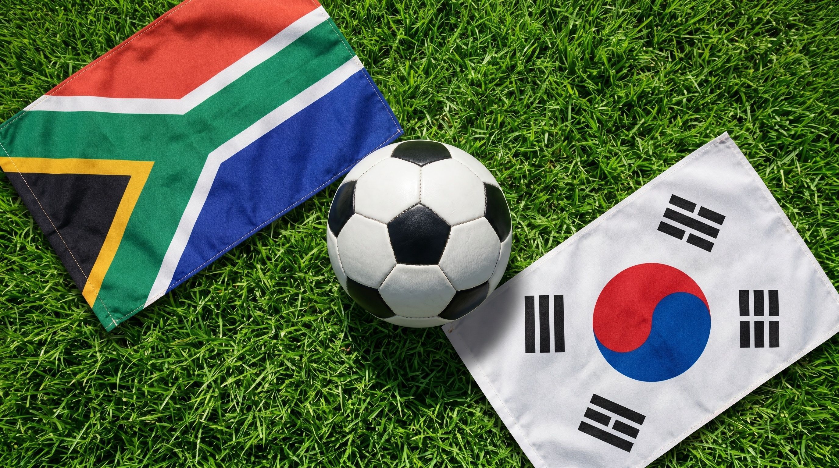 soccer ball resting on a lush green field, flanked by the national flags of South Africa and South Korea