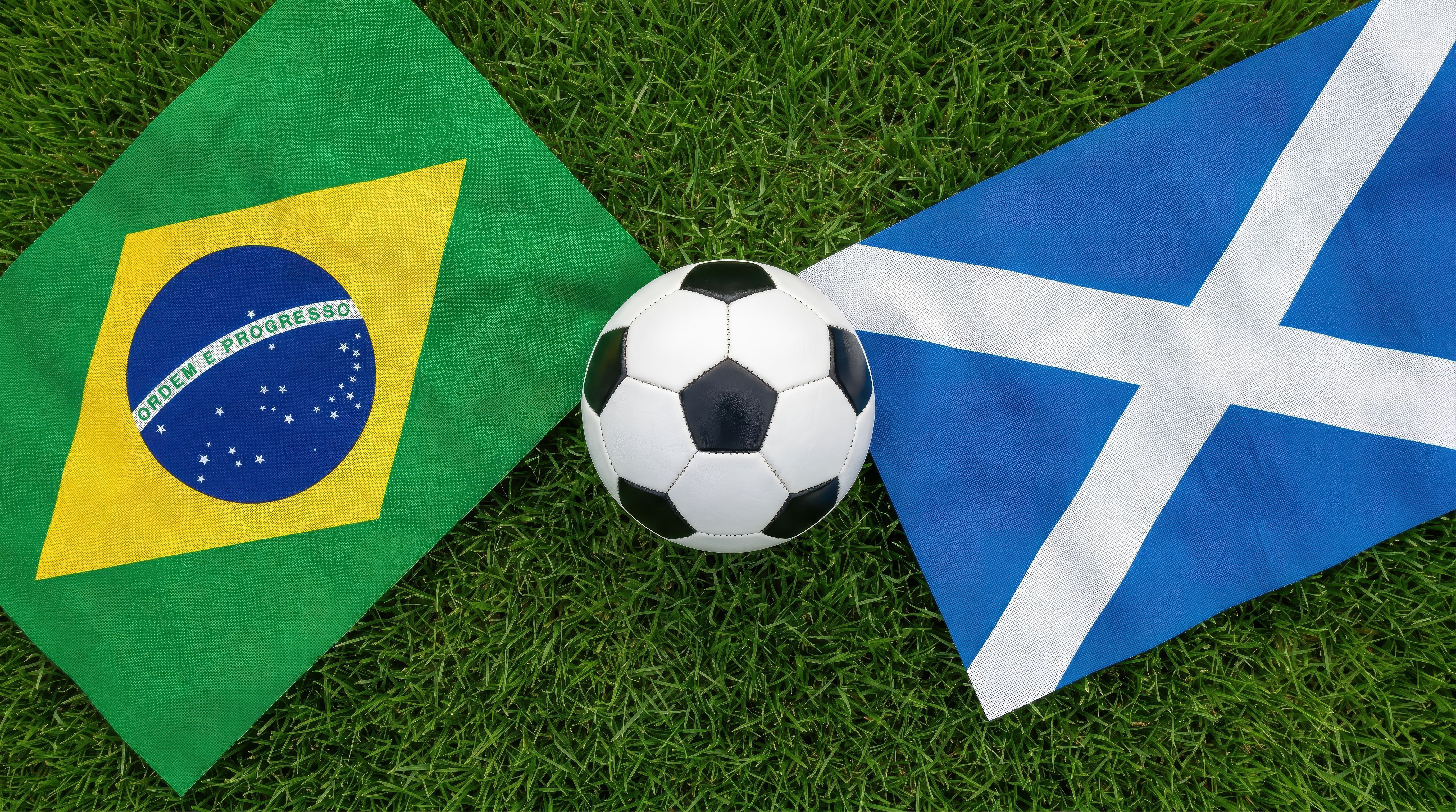 Top view international football concept featuring Scotland and Brazil national flags on green grass pitch with central soccer ball, global sports competition background scene
