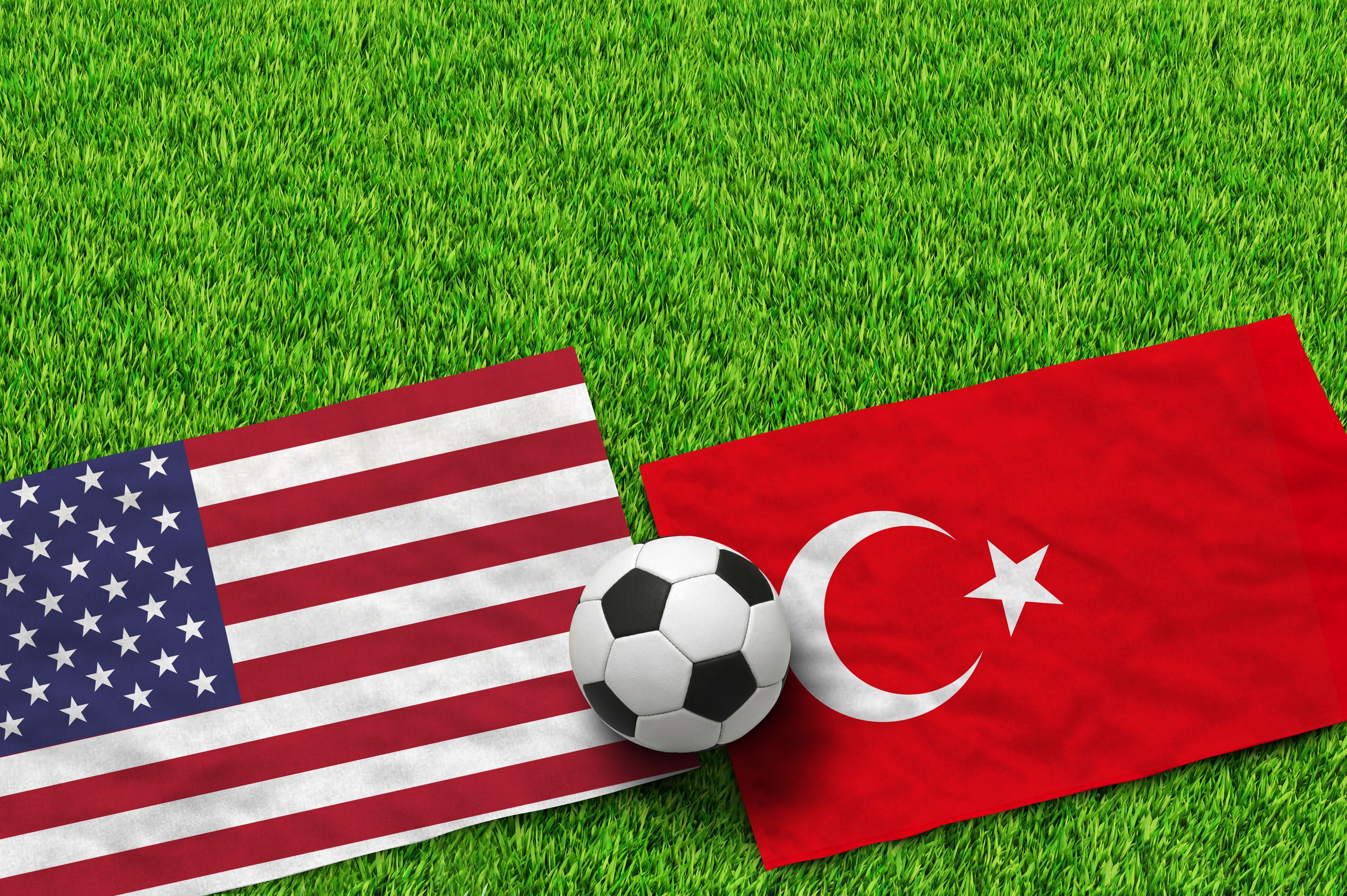 American and Turkish flags with a soccer ball on green grass